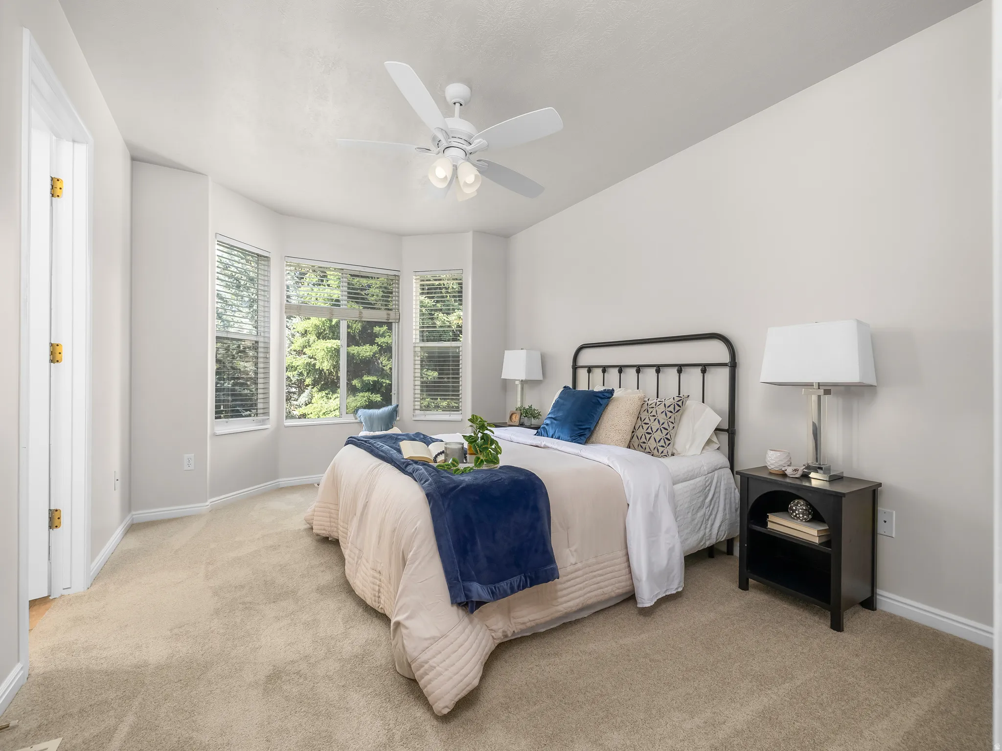 Carpeted room featuring a bay window, ceiling fan, white walls, and white trim