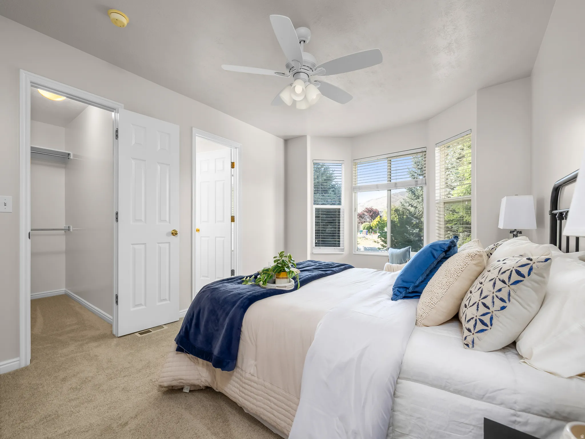 Carpeted bedroom featuring a bay window, ceiling fan with integrated lighting, and a closet with shelving and hanging rods