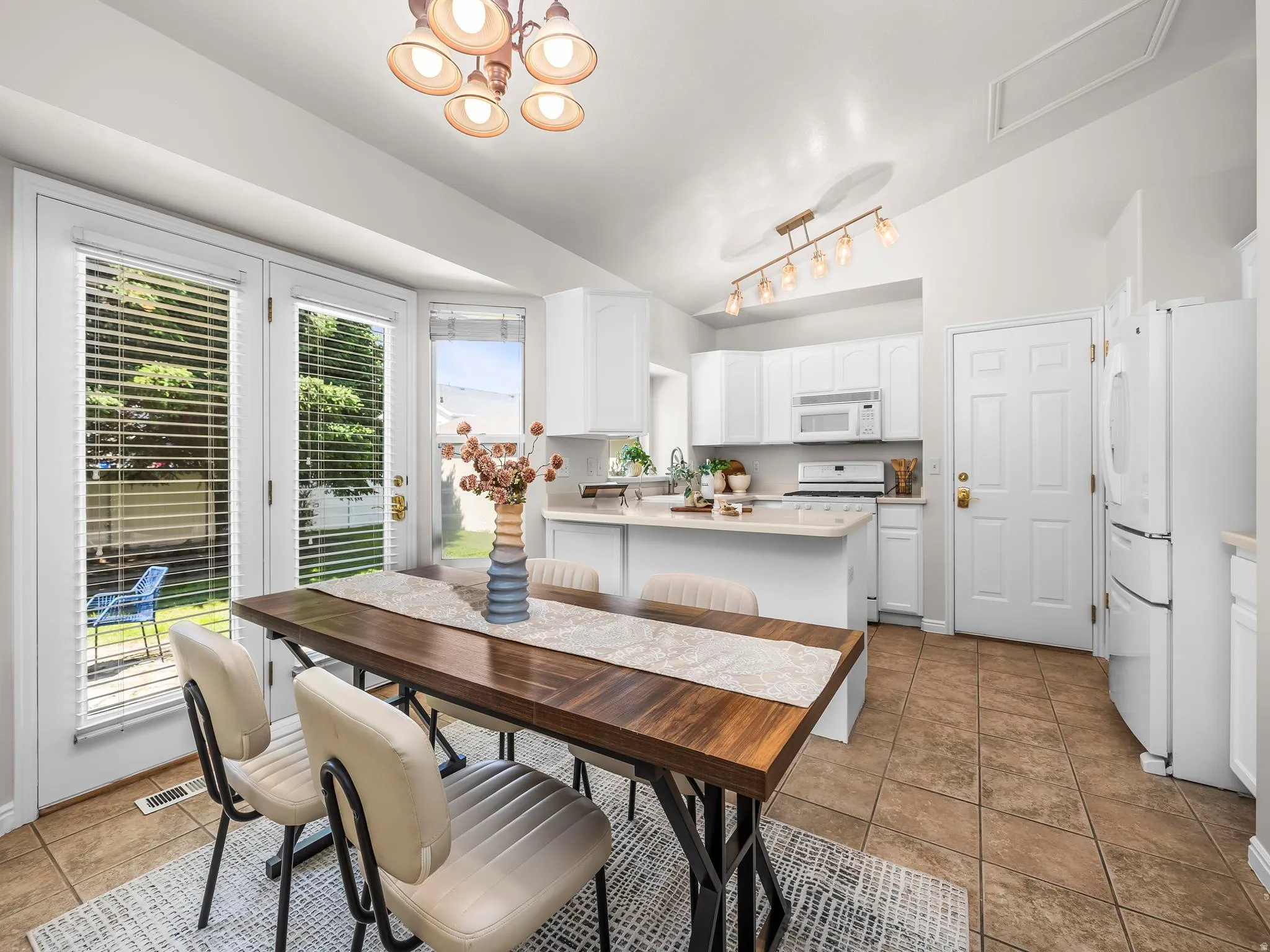 Kitchen and dining area featuring vaulted ceilings, tile flooring, white cabinetry, a kitchen island, and double French doors opening to the exterior