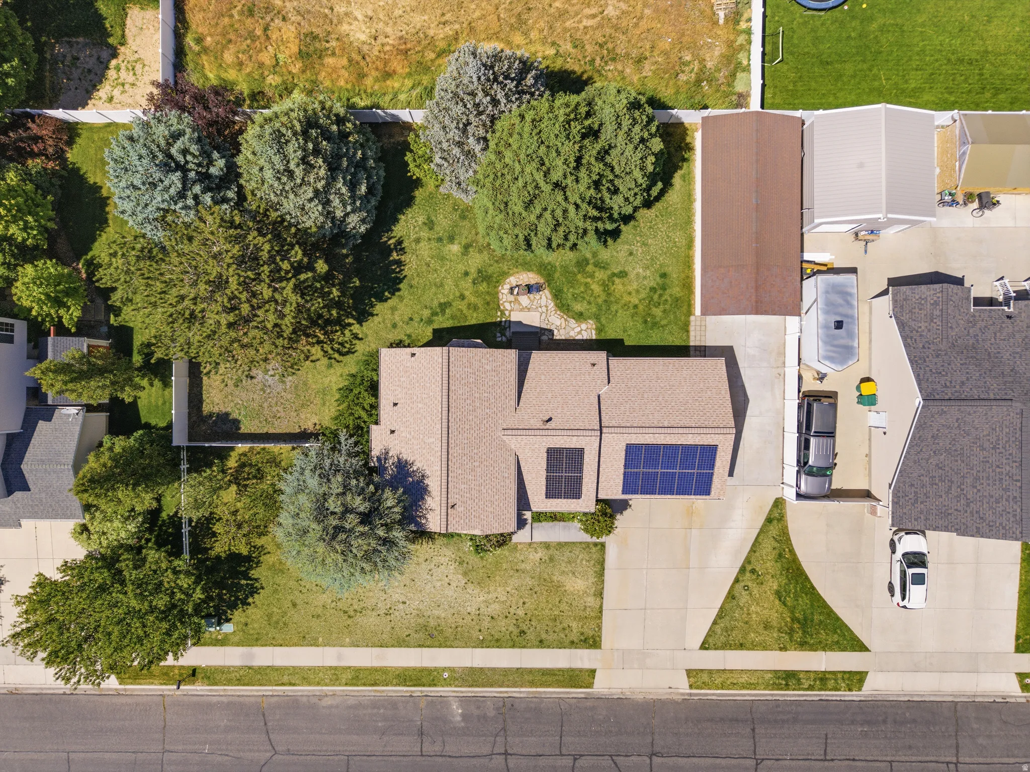 Residential property featuring a shingle roof, solar panels, and an extended concrete driveway