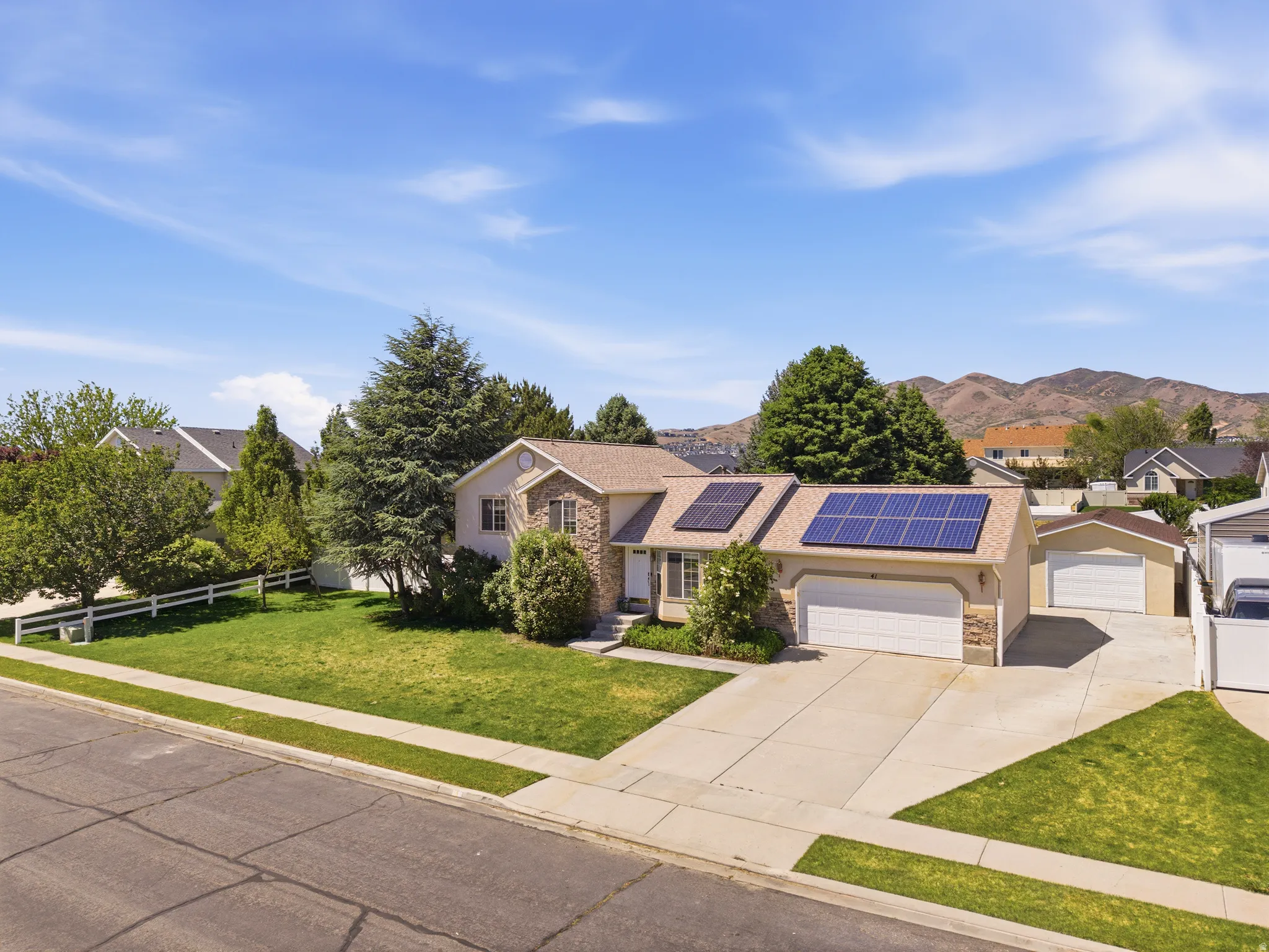 Single-family residence featuring a stone and stucco exterior, prominent solar panels, an attached two-car garage, and an additional detached garage