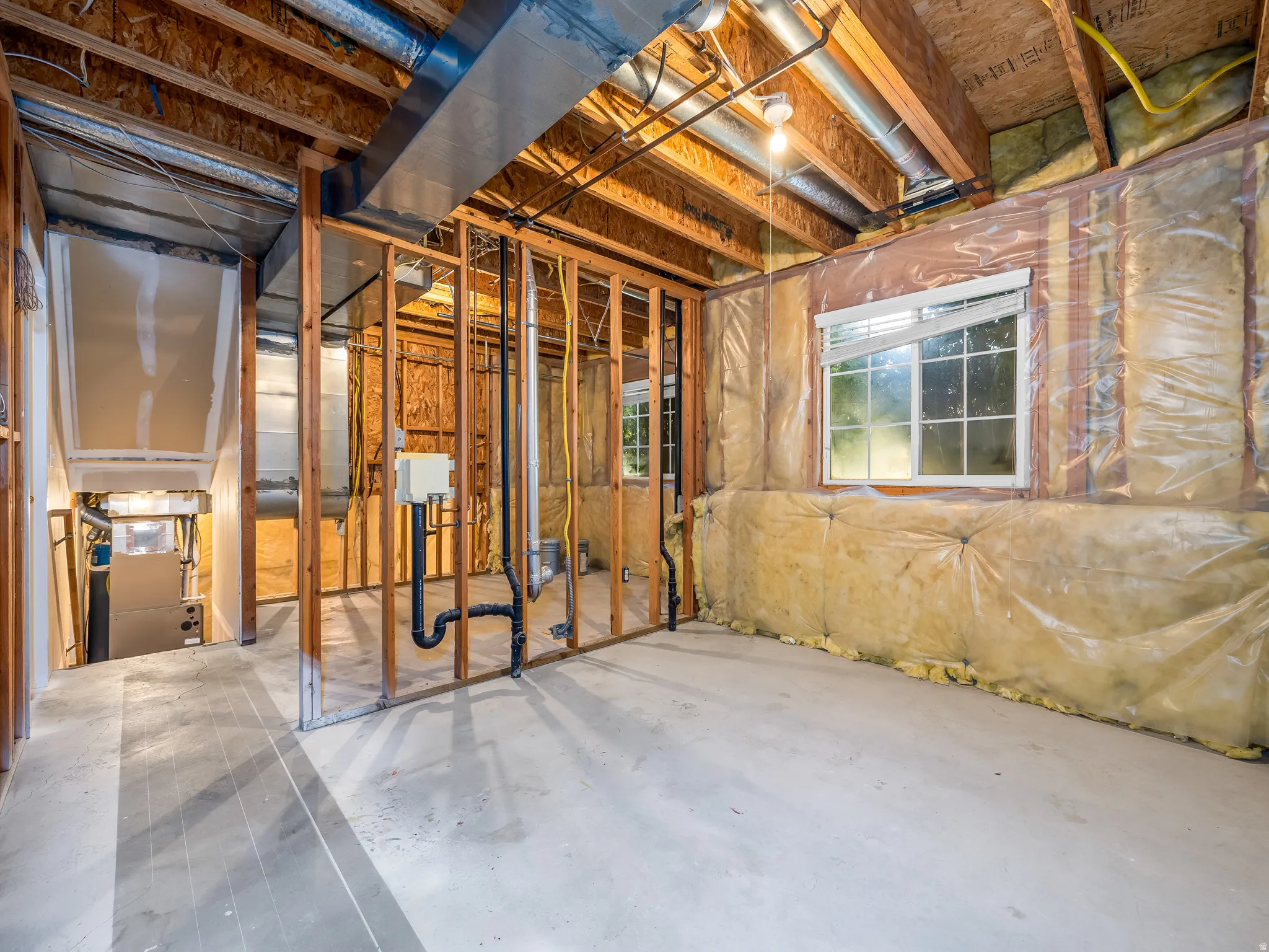 Unfinished basement space featuring exposed wooden framing, visible ductwork, and concrete flooring