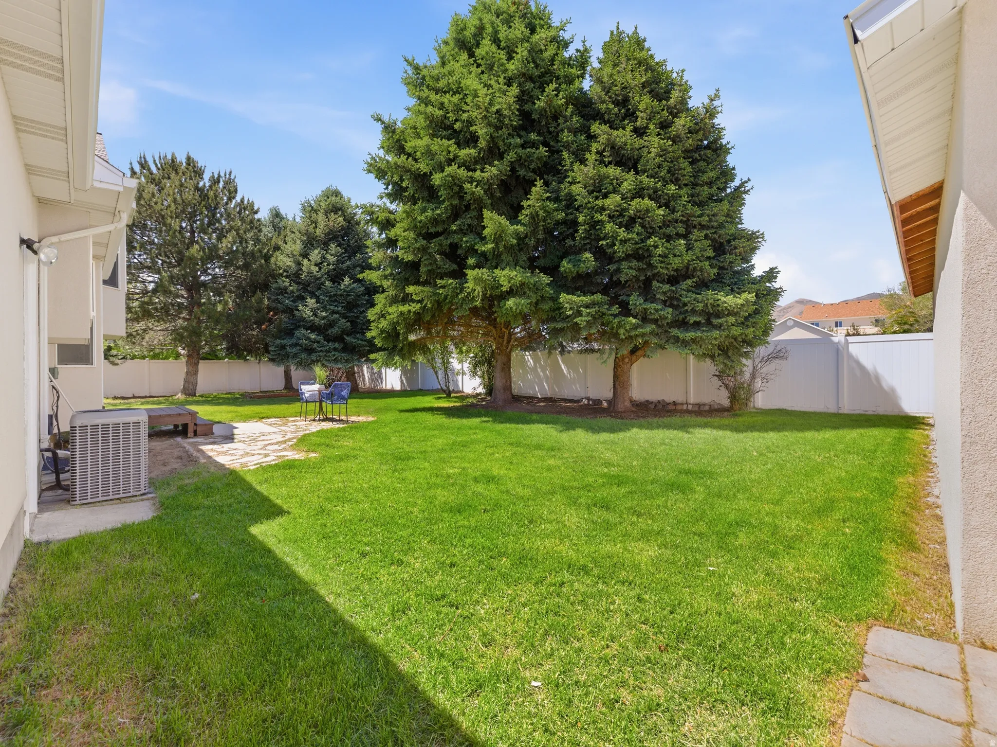 Expansive lawn area featuring mature evergreen trees and a white privacy fence