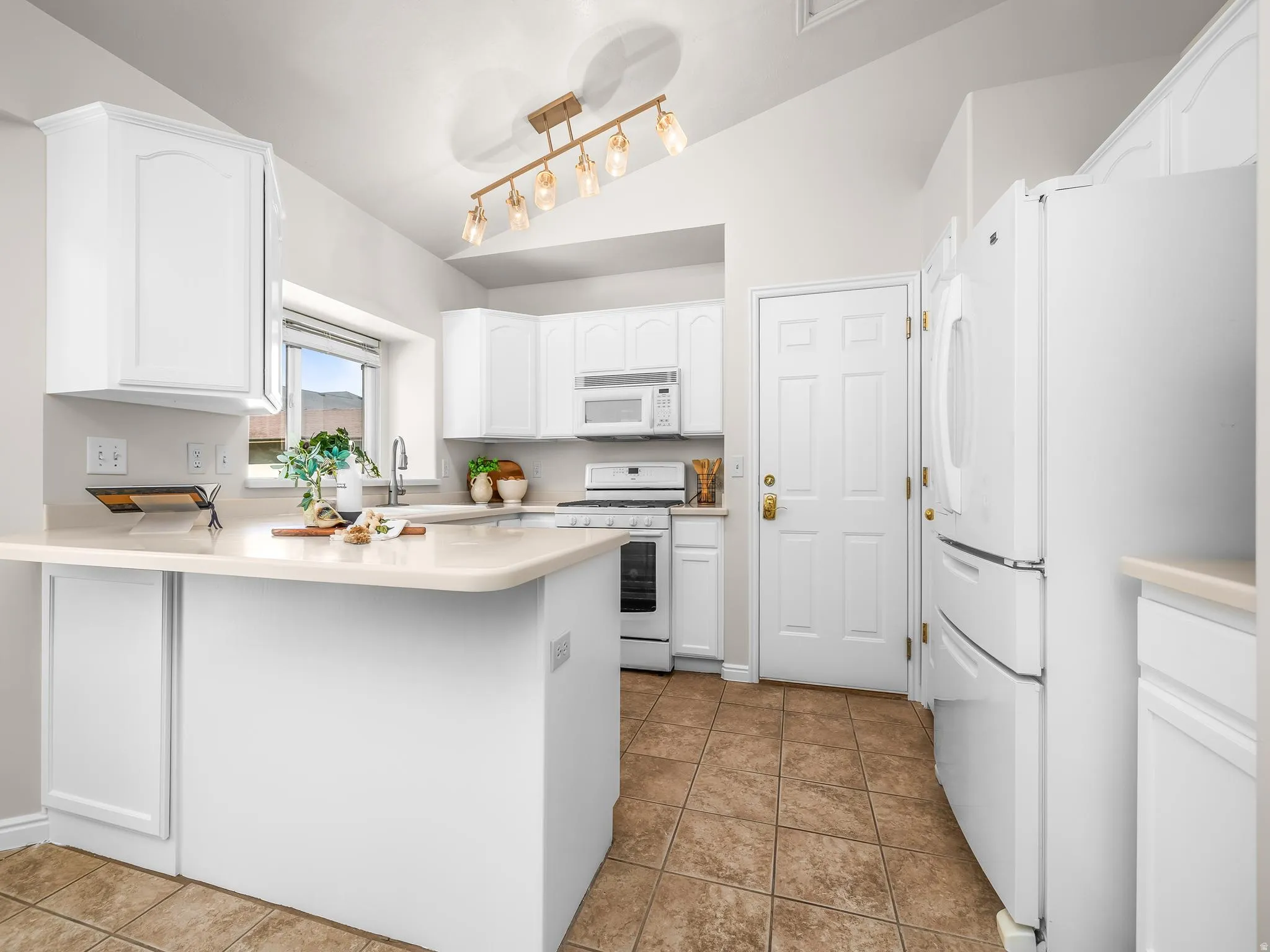 Kitchen featuring white cabinetry, light countertops, integrated white appliances, and a vaulted ceiling with a contemporary light fixture