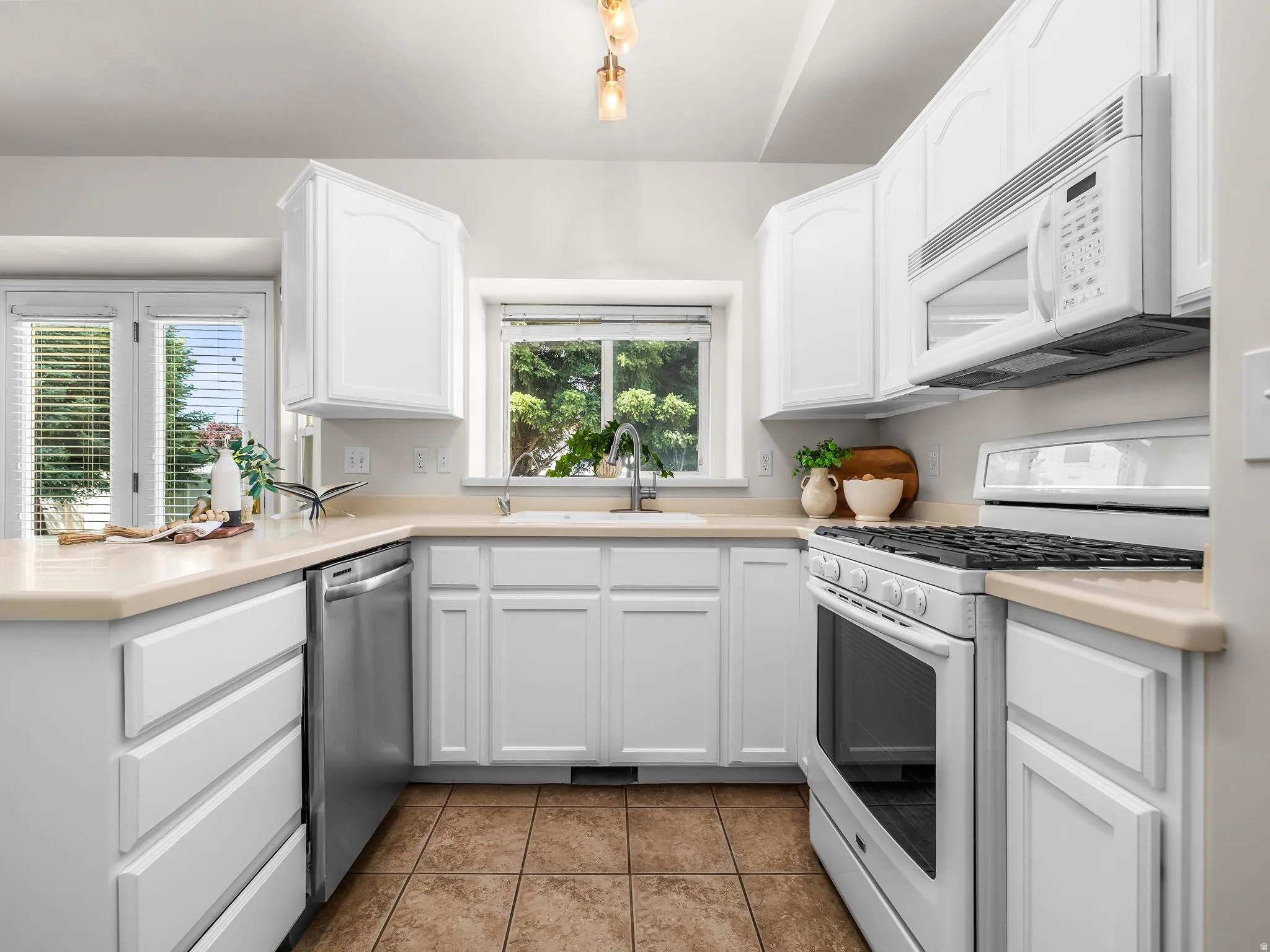 Bright kitchen featuring white cabinetry, light countertops, stainless steel dishwasher, a window over the sink, and tile flooring