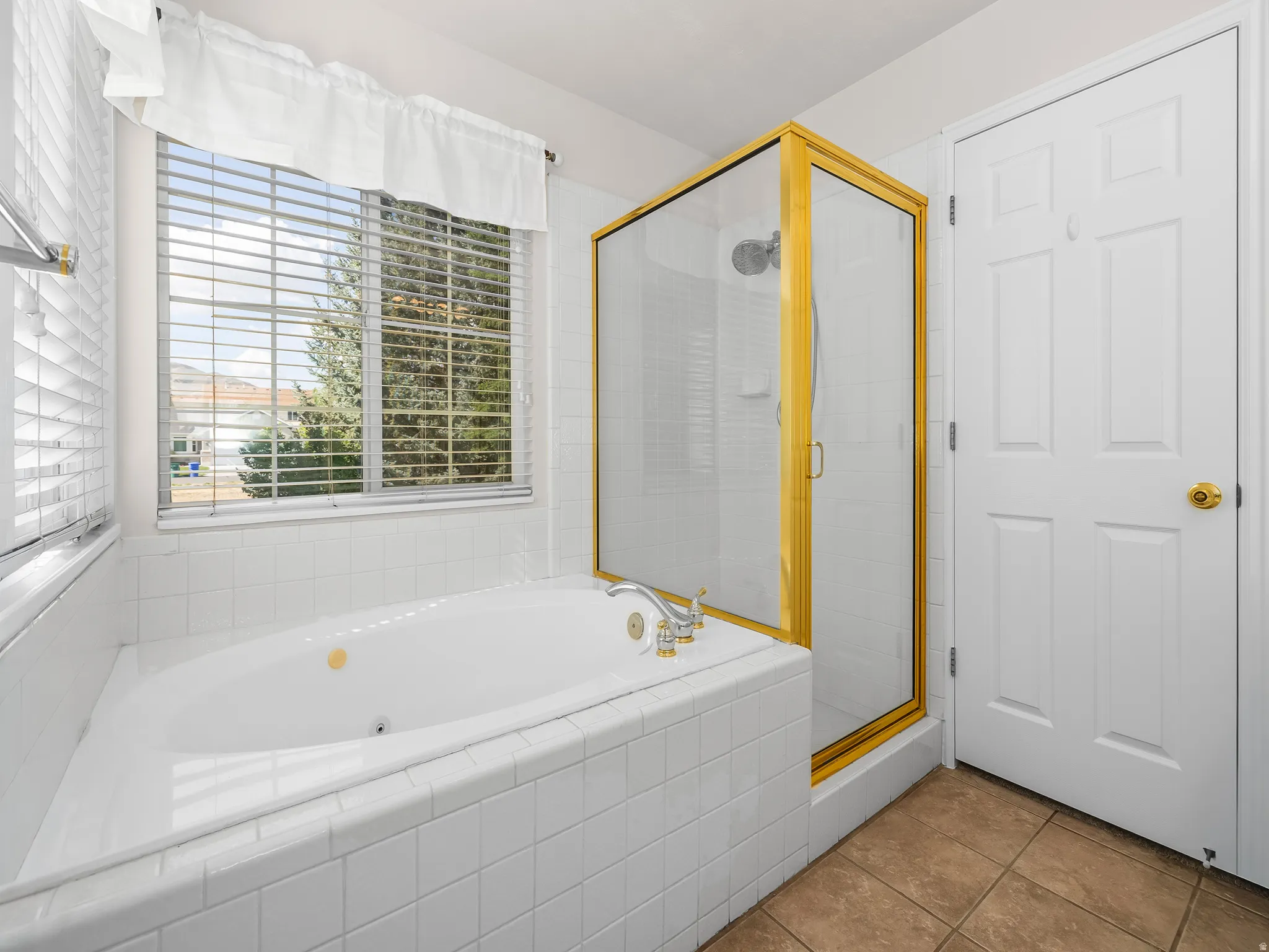 Corner jetted tub set within a tiled surround, complemented by a separate glass-enclosed shower with gold-tone framing and hardware