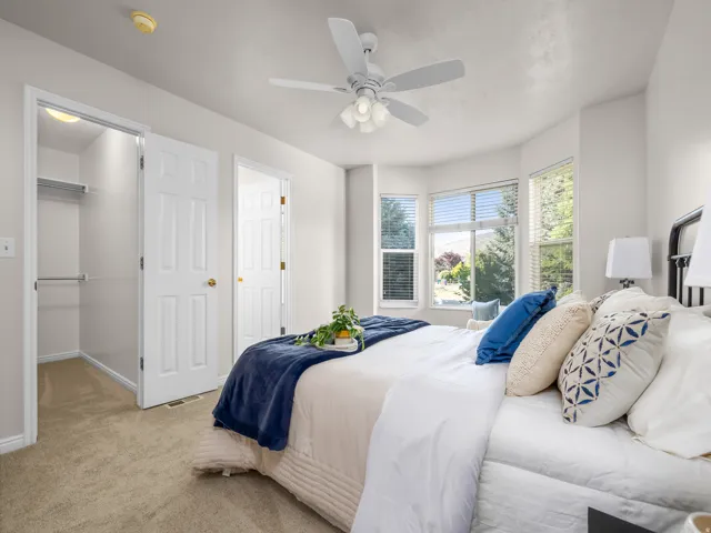 Carpeted bedroom featuring a bay window, ceiling fan with integrated lighting, and a closet with shelving and hanging rods