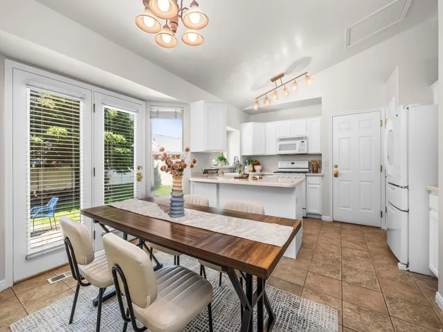 Kitchen and dining area featuring vaulted ceilings, tile flooring, white cabinetry, a kitchen island, and double French doors opening to the exterior