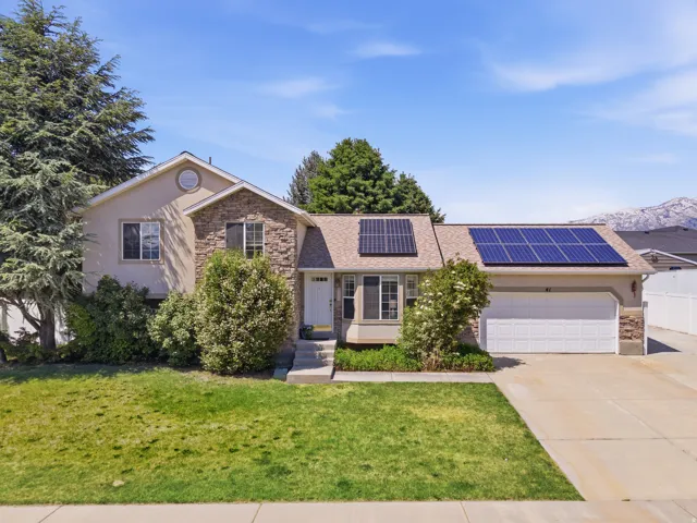 Two-story residence featuring a combination of stucco and stone veneer siding, an attached two-car garage, multiple solar panel arrays, and mature landscaping