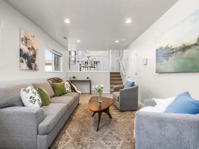 Spacious living area featuring light-toned walls, recessed lighting, wood-finish flooring with an area rug, and an open stairwell with white railings