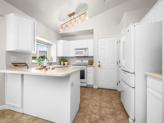 Kitchen featuring white cabinetry, light countertops, integrated white appliances, and a vaulted ceiling with a contemporary light fixture