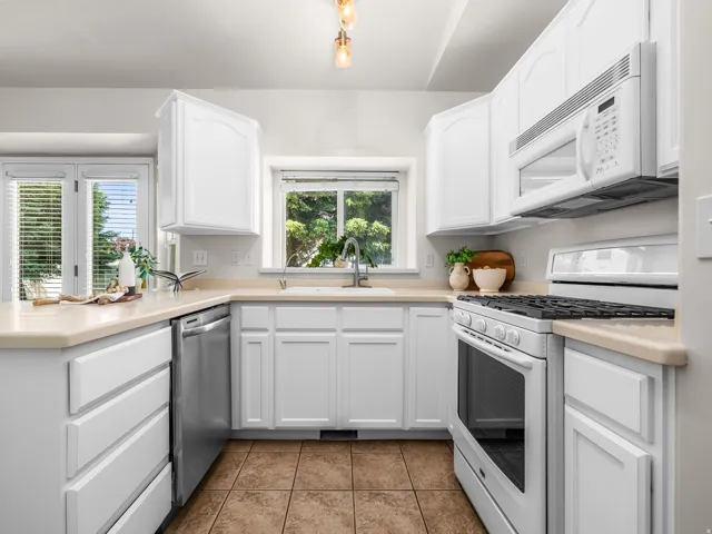 Bright kitchen featuring white cabinetry, light countertops, stainless steel dishwasher, a window over the sink, and tile flooring