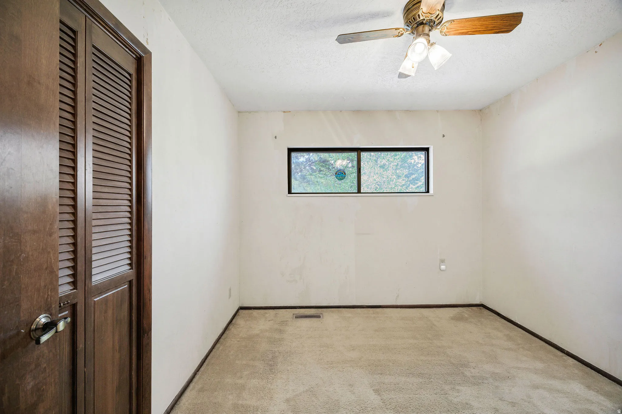 Carpeted room featuring a ceiling fan, horizontal window, and bifold closet doors