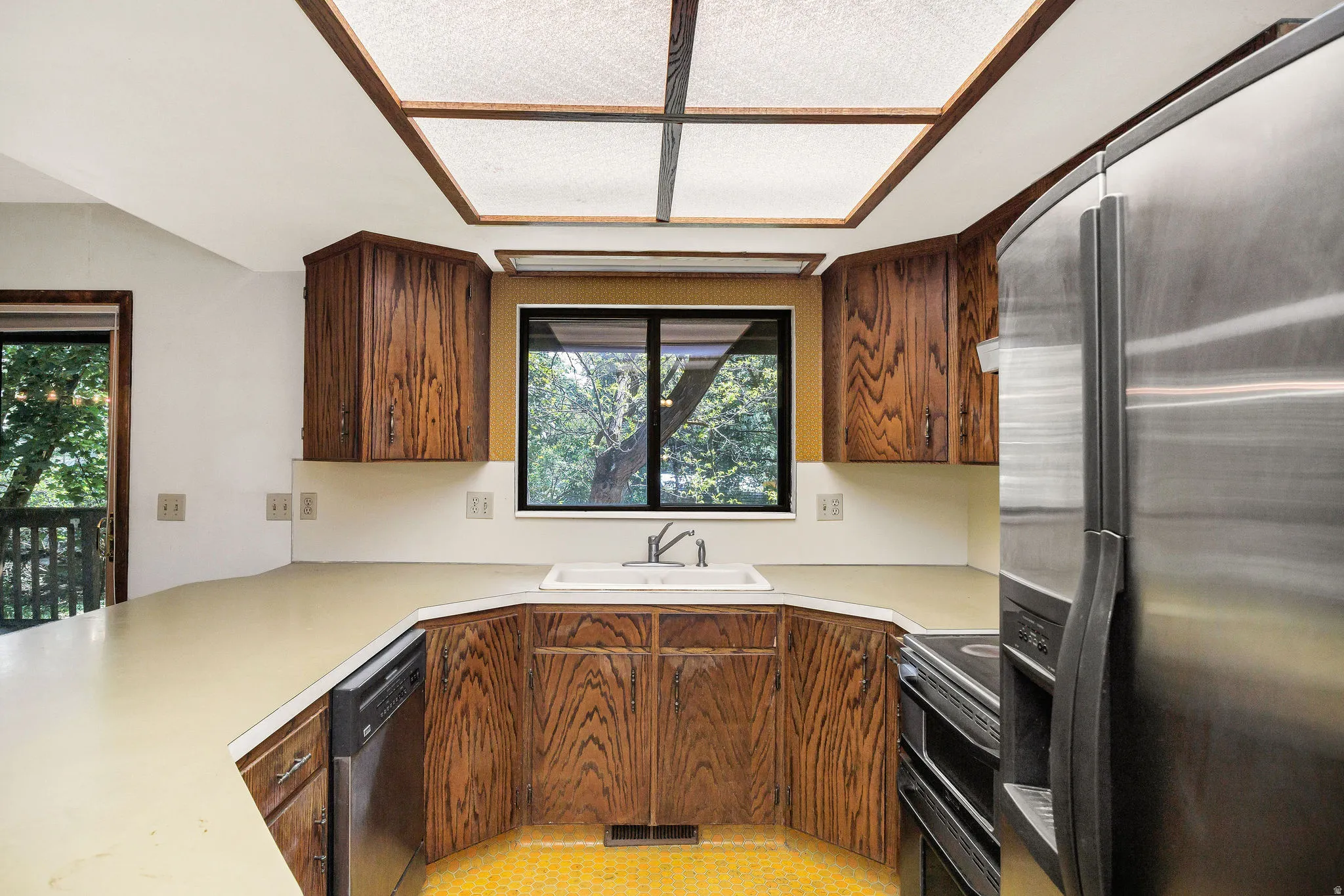 U-shaped kitchen featuring wood cabinetry, light-toned countertops, and a white sink below a window