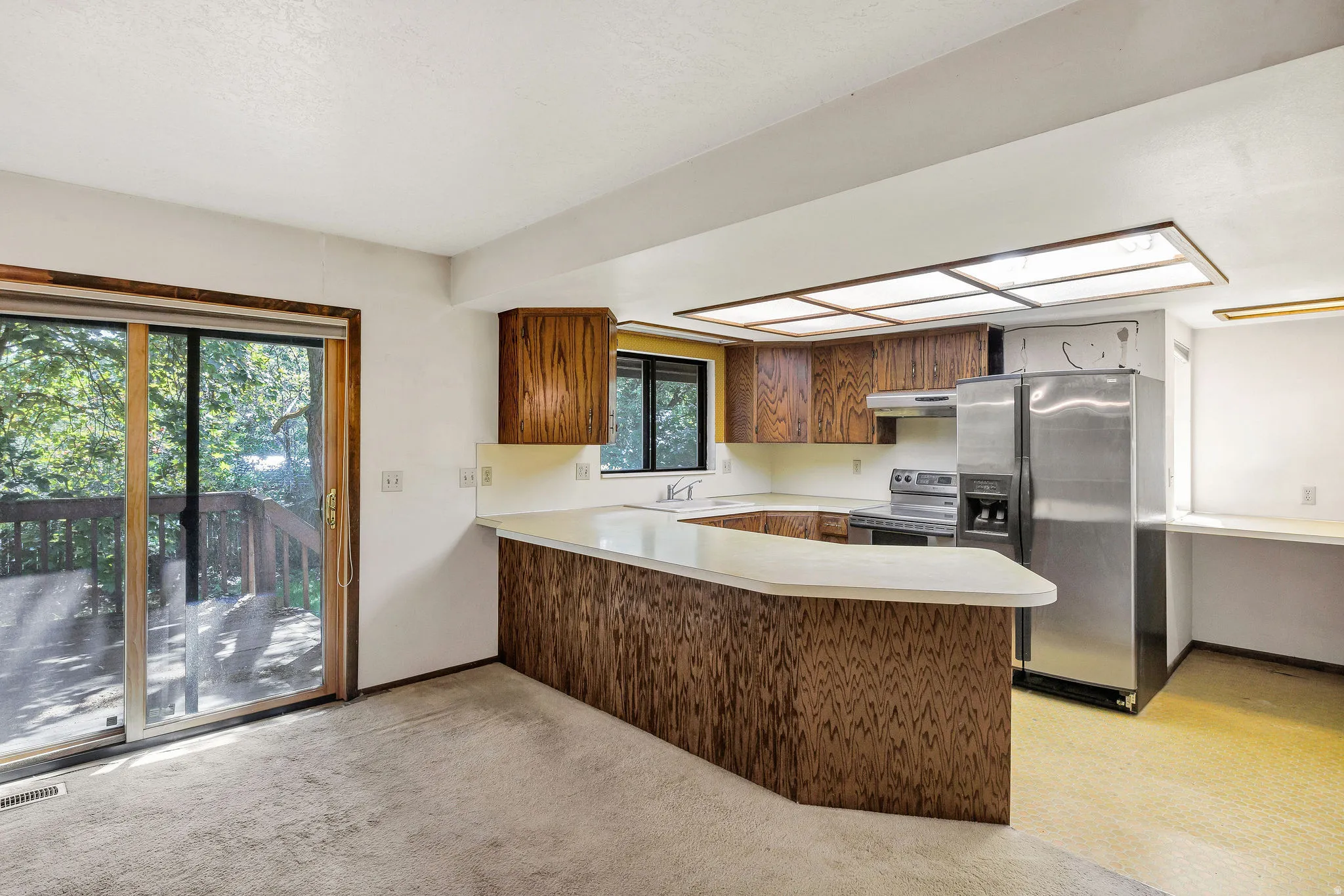 Open concept kitchen featuring wood cabinetry, white countertops, stainless steel appliances, and a built-in desk area