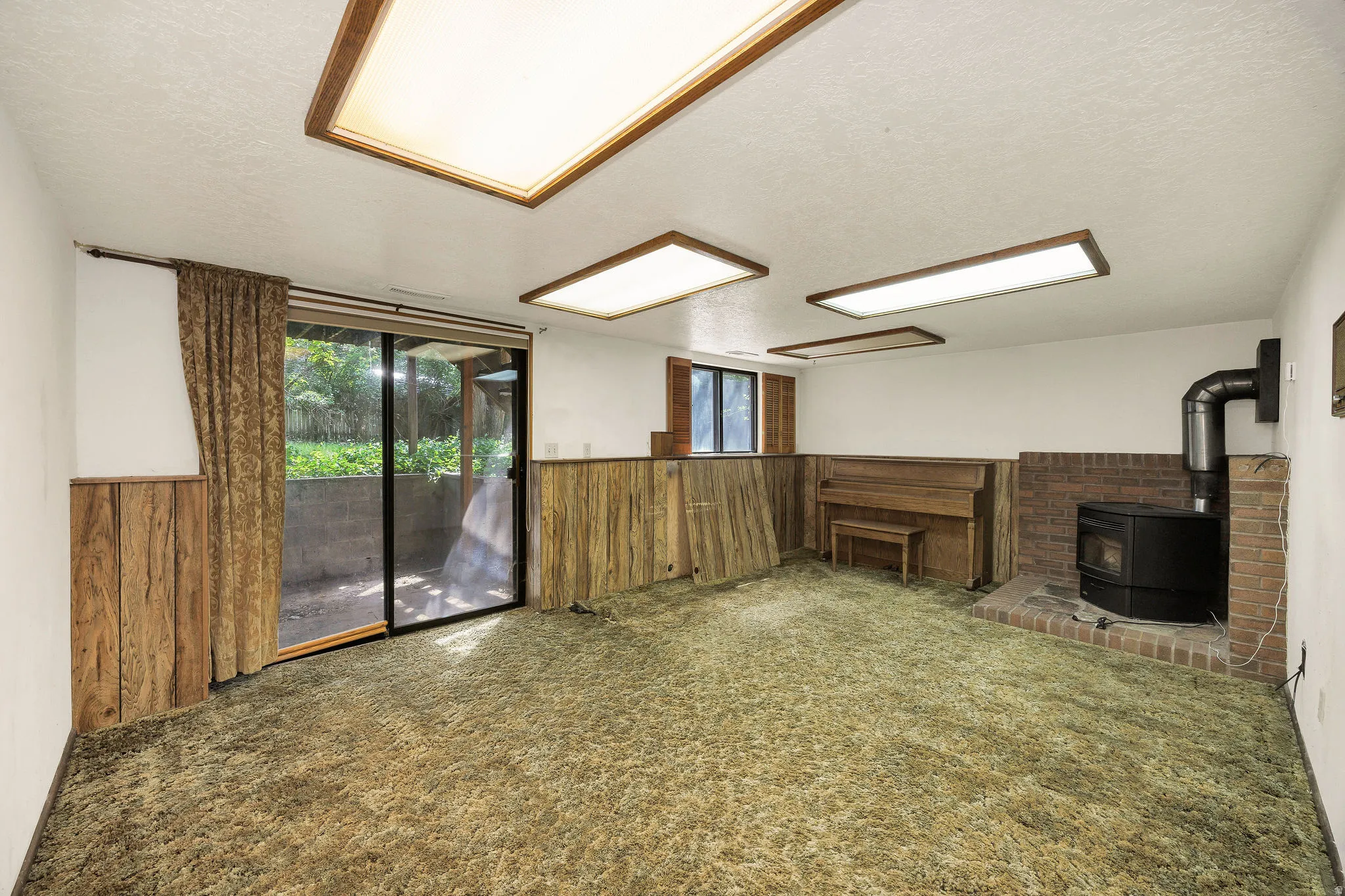 Spacious interior room featuring a brick-surround wood-burning stove, wood paneling, and a large sliding glass door opening to the exterior