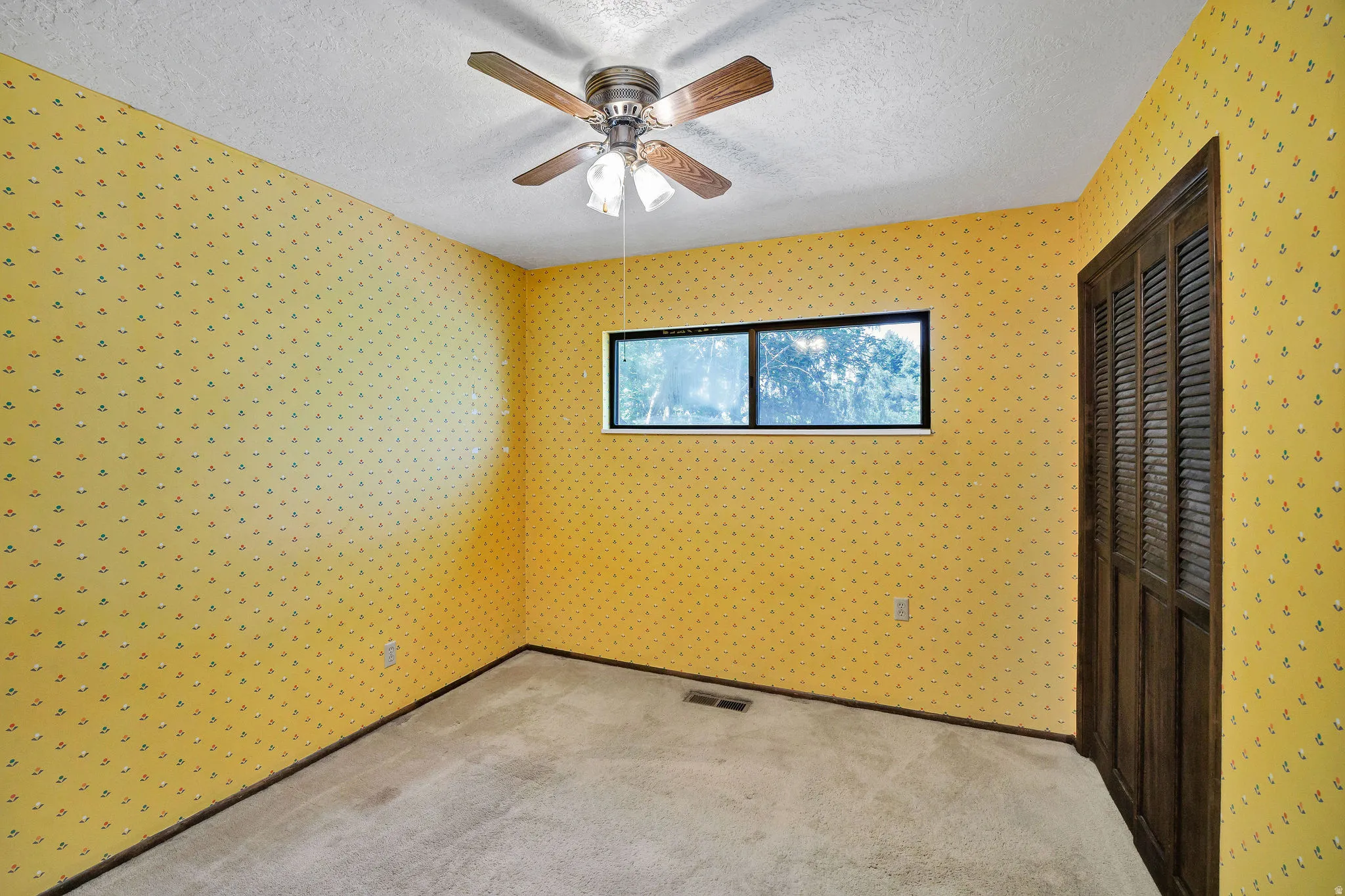 Carpeted room with a ceiling fan, a horizontal window, and bifold louvered closet doors