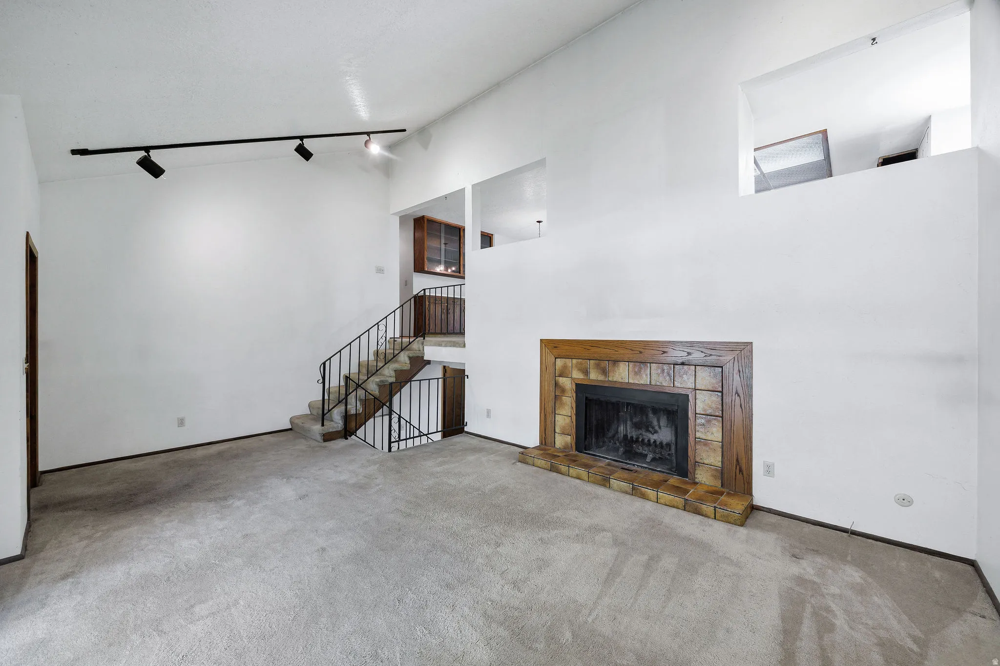 Vaulted ceiling living area featuring a wood-surround fireplace with a stone tile hearth, track lighting, and a staircase with an iron railing