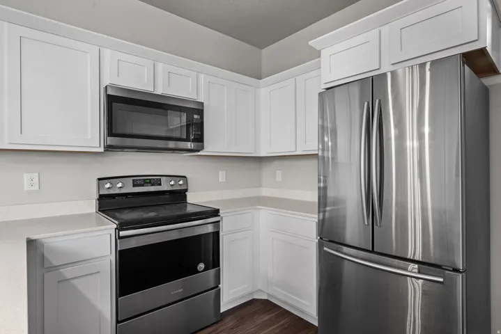 Modern kitchen featuring white cabinetry with brushed nickel hardware, light-toned countertops, and stainless steel appliances