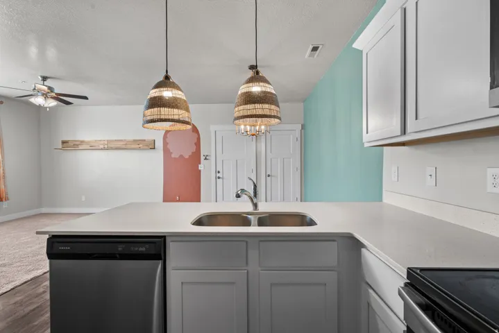 Kitchen island featuring a double basin stainless steel sink, a stainless steel dishwasher, light-colored countertops, and pendant lighting with woven shades