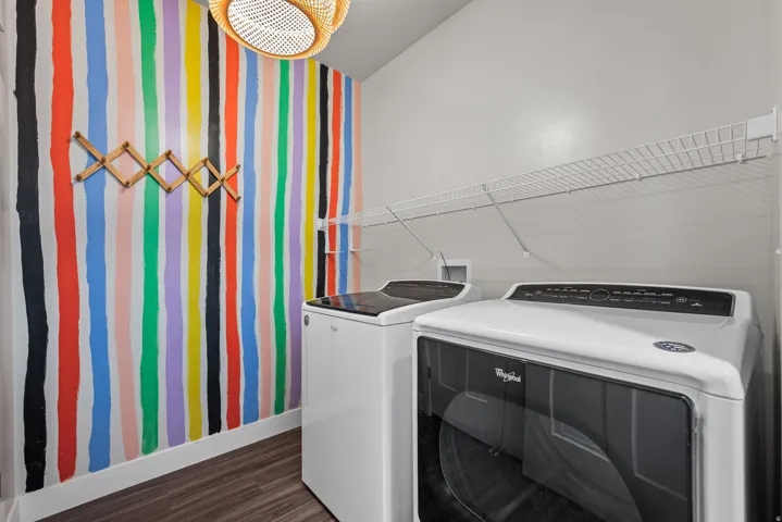 Laundry area featuring a vibrant striped accent wall, wood-finish flooring, a decorative expandable wooden rack, and wire shelving