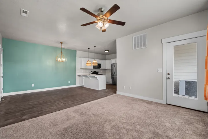 Open-concept living area featuring a decorative accent wall, wood-finish flooring, and plush carpeting