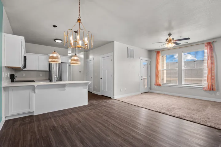 Open-concept living space featuring wood-finish flooring, a carpeted area, and a kitchen with white cabinetry