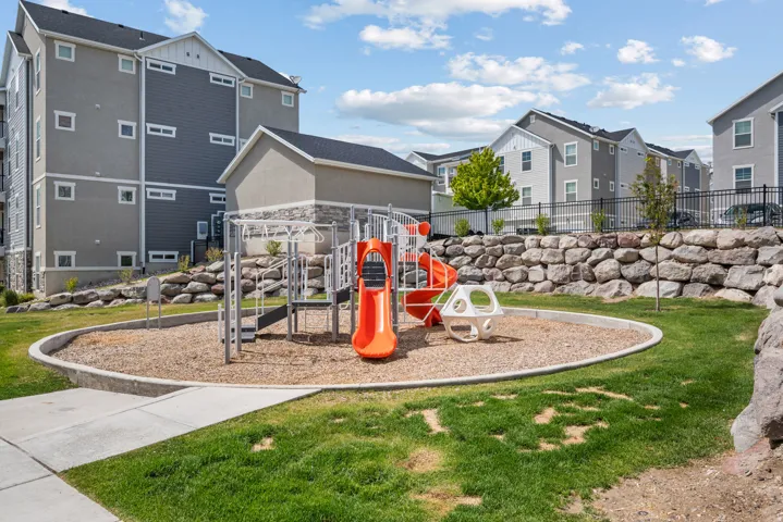 Property playground featuring a slide, monkey bars, and climbing structures on a wood chip surface, surrounded by a concrete border