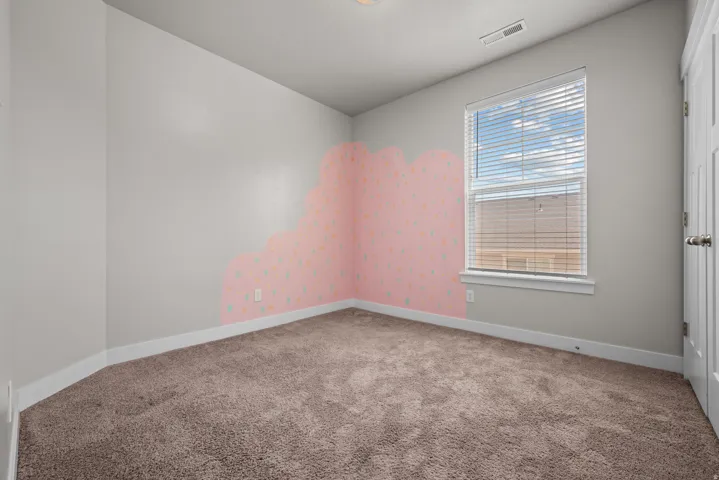 Carpeted room featuring a single window with blinds, a white door, and light gray walls with a decorative accent