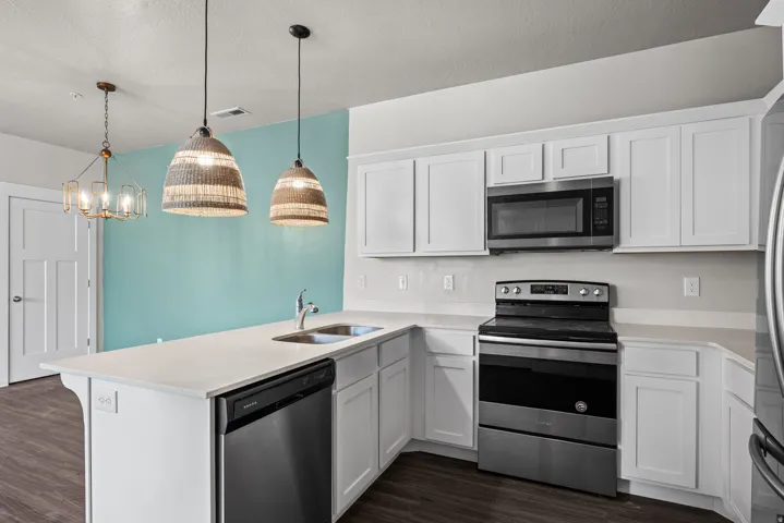 Kitchen featuring white shaker-style cabinetry, light-toned countertops, stainless steel appliances, and dark wood-finish flooring