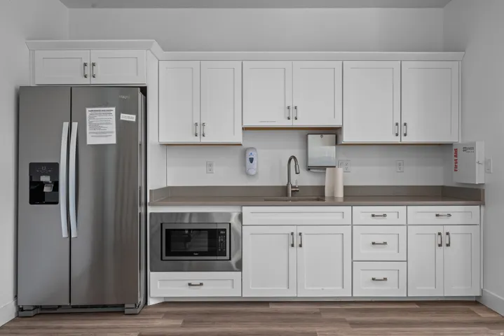 Kitchenette featuring white shaker-style cabinetry, a stainless steel side-by-side refrigerator, a built-in microwave, wood-finish flooring, and a countertop with an integrated sink