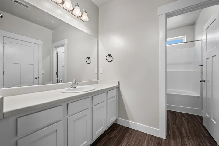 Bathroom featuring a double vanity with white cabinetry, an integrated sink, and a large wall-mounted mirror