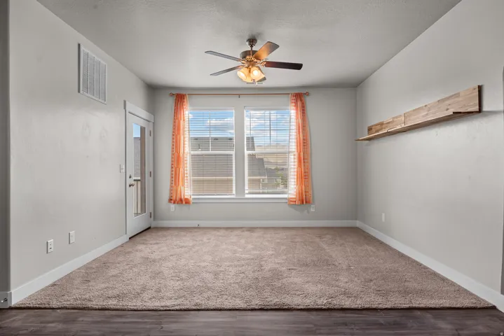 Carpeted interior space featuring a ceiling fan with integrated lighting, wood-finish flooring border, a glass-paneled door, and a multi-pane window