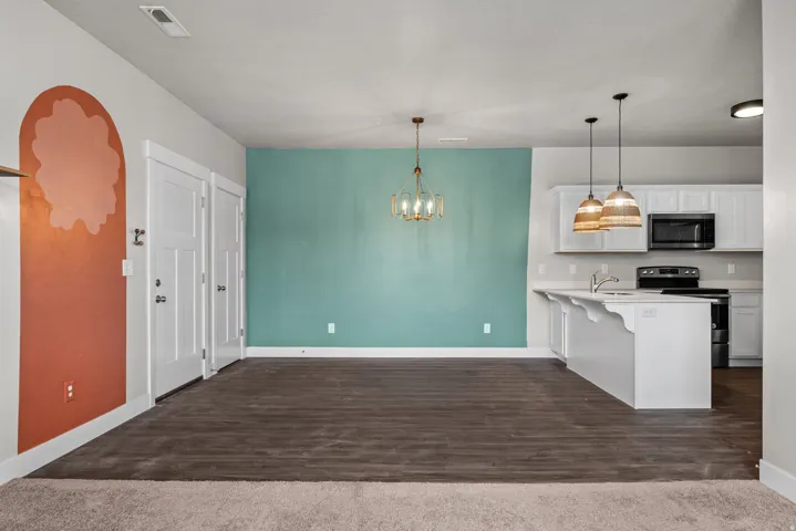 Open-concept living space featuring wood-finish flooring, a contemporary chandelier, and a kitchen island with pendant lighting