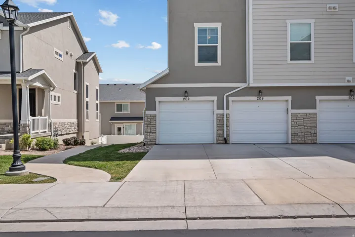 Modern townhome exterior featuring an attached garage, light gray siding, stone accents, and a concrete driveway