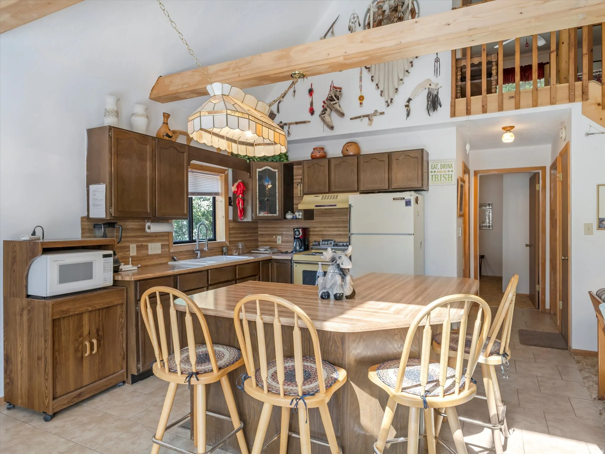 Kitchen featuring wood-finish cabinetry, tile flooring, a built-in double basin sink, and an island with seating