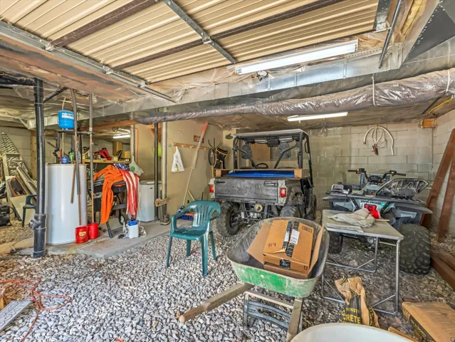 Utility space featuring exposed metal ceiling joists, fluorescent lighting fixtures, concrete block walls, and a gravel floor