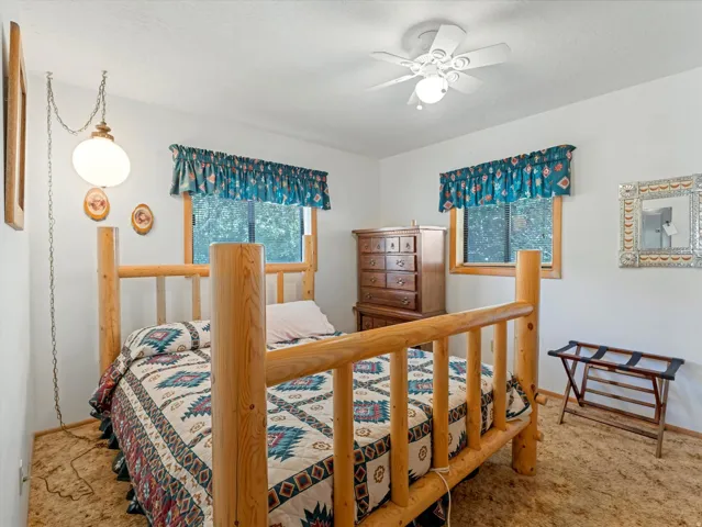 Bedroom featuring a ceiling fan with integrated lighting, a hanging pendant light fixture, two windows with valances, and light-colored wall paint