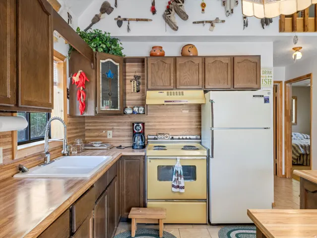 Kitchen featuring wood-finish countertops and backsplash, coordinating wood cabinetry, a white drop-in sink with a gooseneck faucet, and light-toned floor tiling