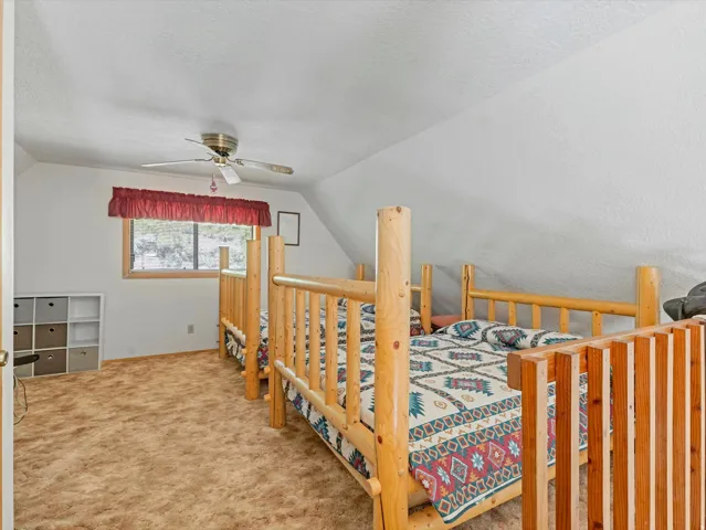 Carpeted room with a pitched ceiling and a window featuring a red valance