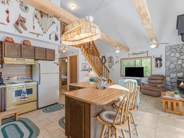 Open-concept living area featuring a kitchen with wood cabinetry, a central island with bar seating, and a living space with a stone fireplace