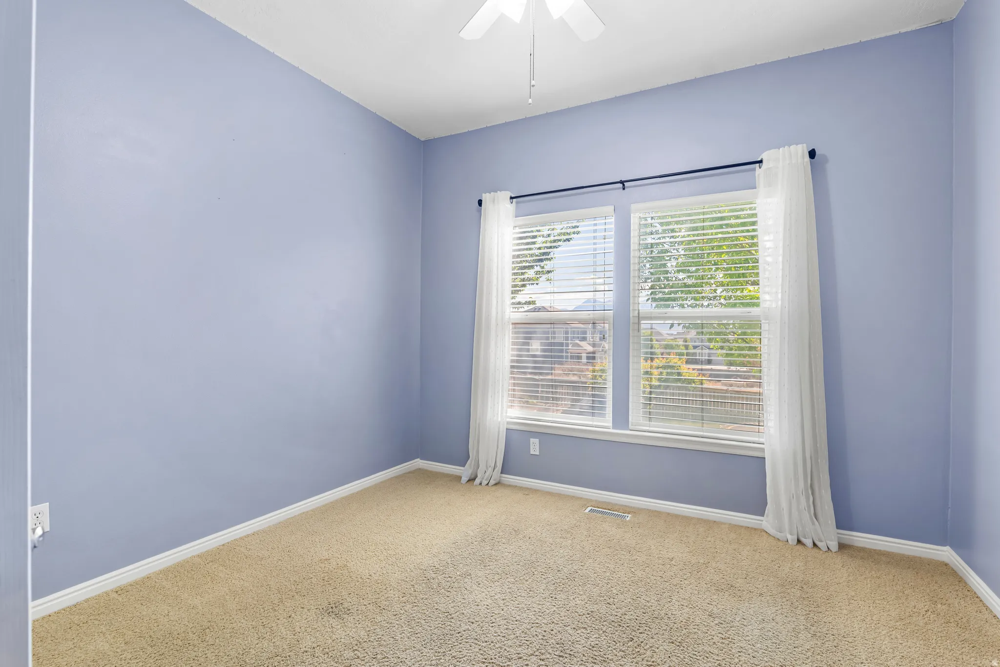 Carpeted room featuring a ceiling fan, dual windows with blinds, and white baseboards