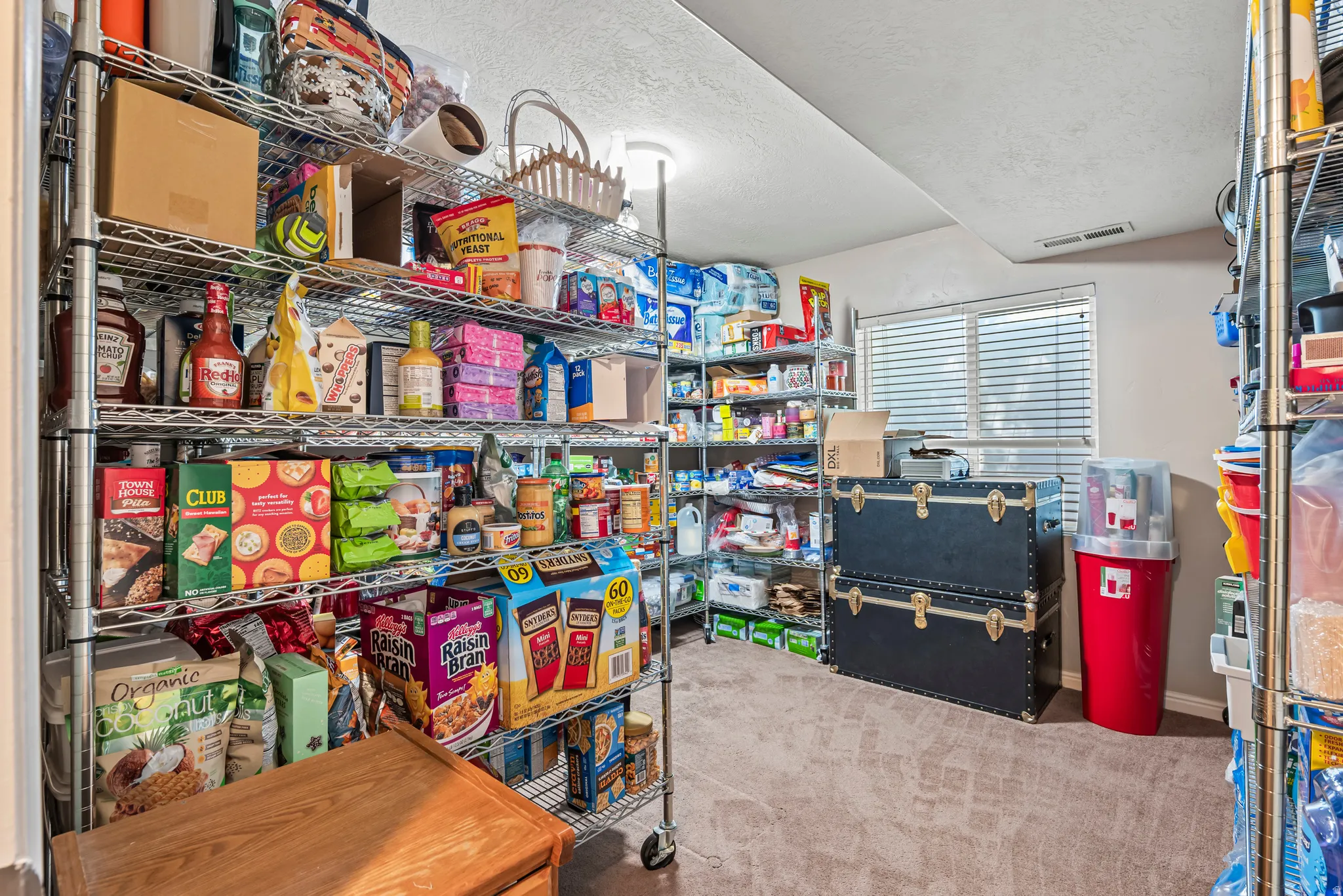 Spacious pantry featuring extensive chrome wire shelving, recessed lighting, a single window with horizontal blinds, and neutral carpet flooring