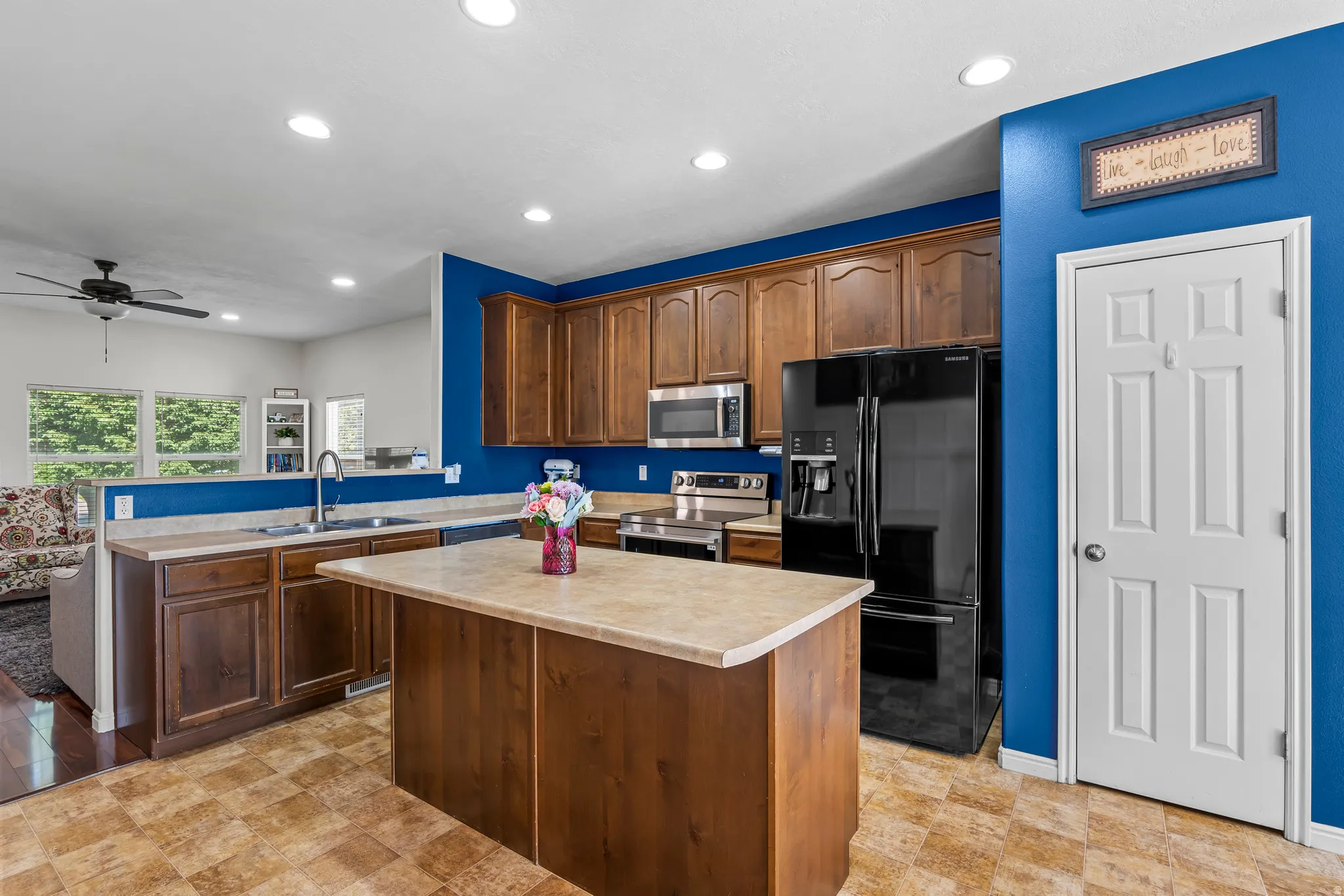 Kitchen featuring a central island, wood-finish cabinetry, stainless steel appliances, and a black refrigerator