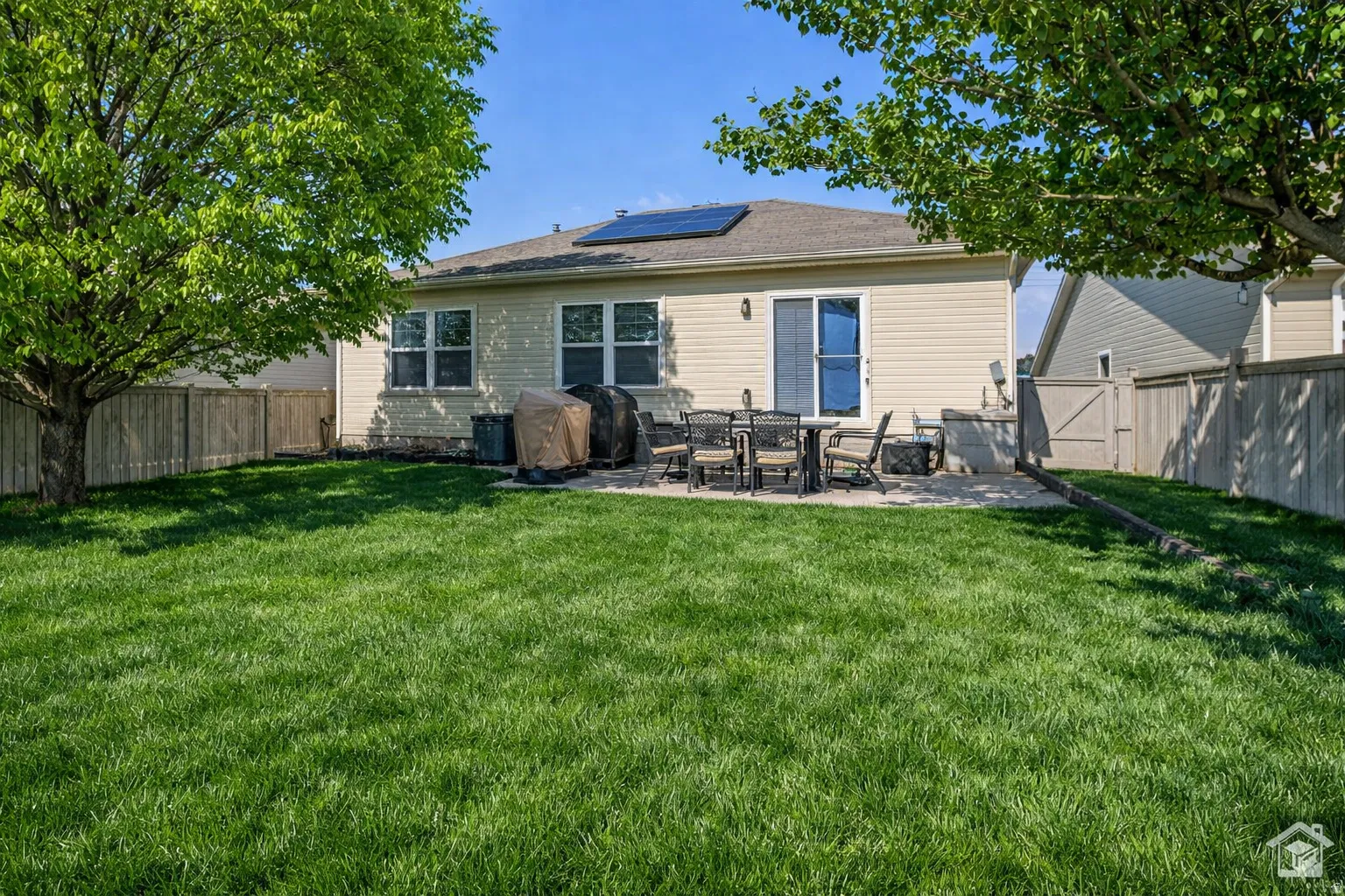 Expansive backyard featuring a lush lawn, mature trees, and a spacious paved patio