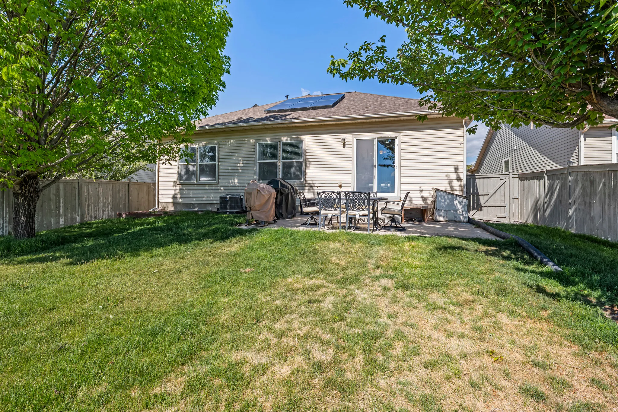 Expansive backyard featuring a concrete patio, vinyl siding exterior, multiple windows, solar panels on the roof, and a sliding glass door