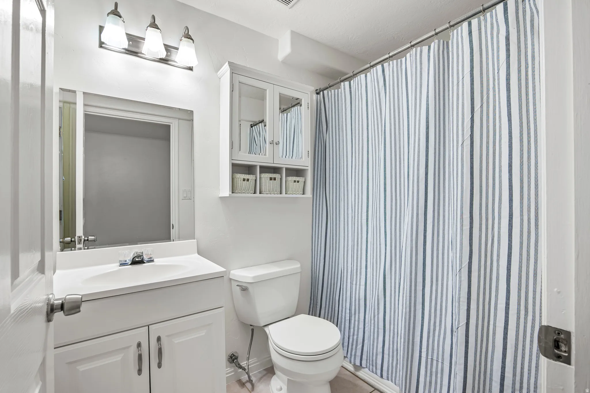 Bathroom featuring a vanity with an integrated sink, a wall-mounted mirror, overhead lighting with three fixtures, a toilet, and a built-in cabinet with glass-fronted doors and open shelving