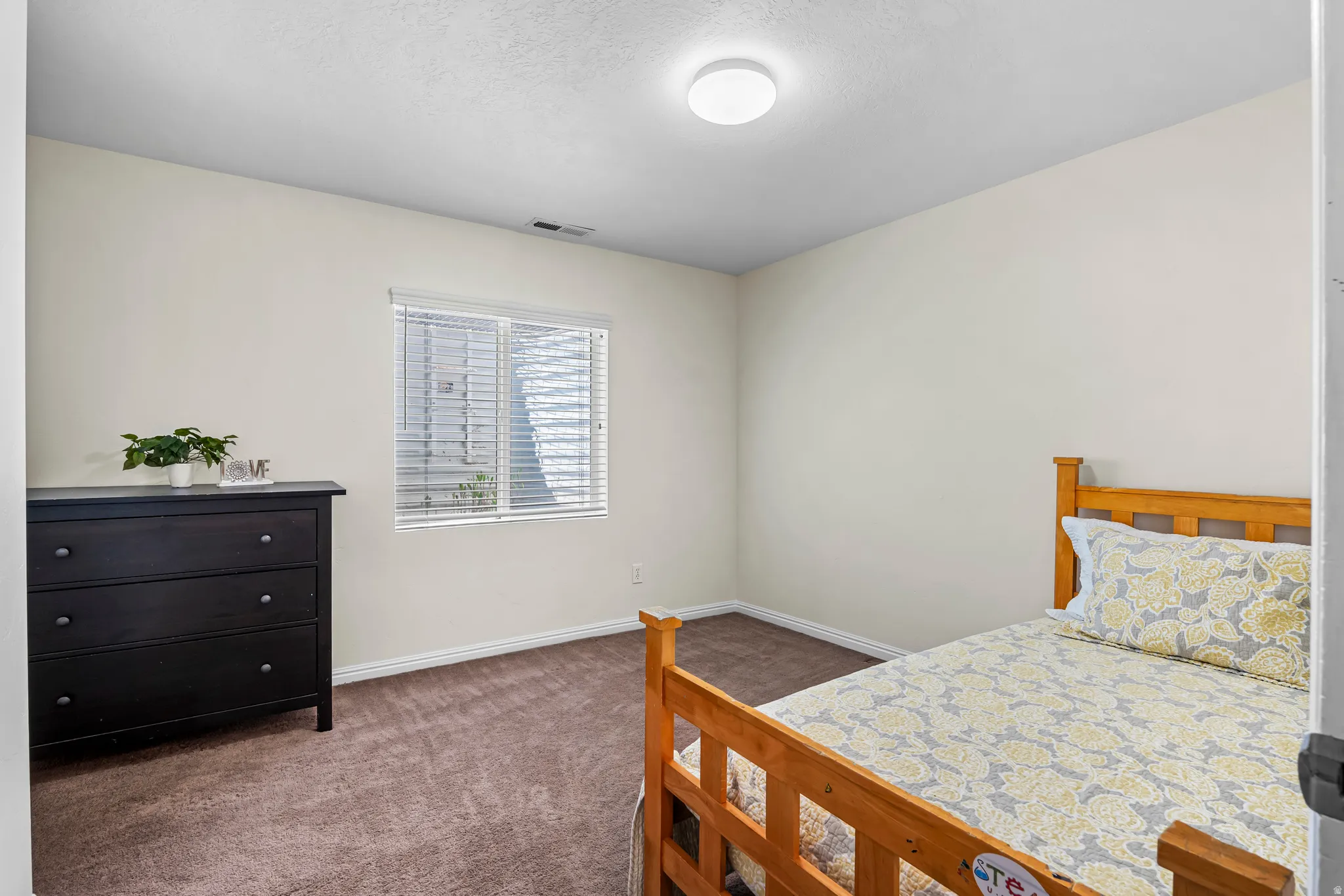 Compact room featuring light-toned walls, brown carpet flooring, and a single window with horizontal blinds