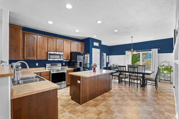Spacious kitchen featuring warm wood cabinetry, stainless steel appliances, a central island, and durable tile-patterned flooring