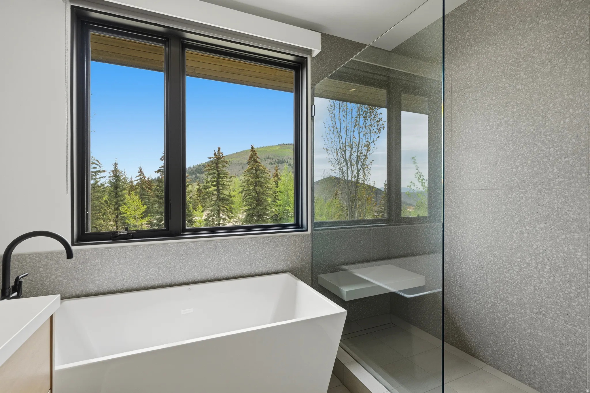 Freestanding soaking tub with a matte black faucet, set against a window with mountain and tree scenery
